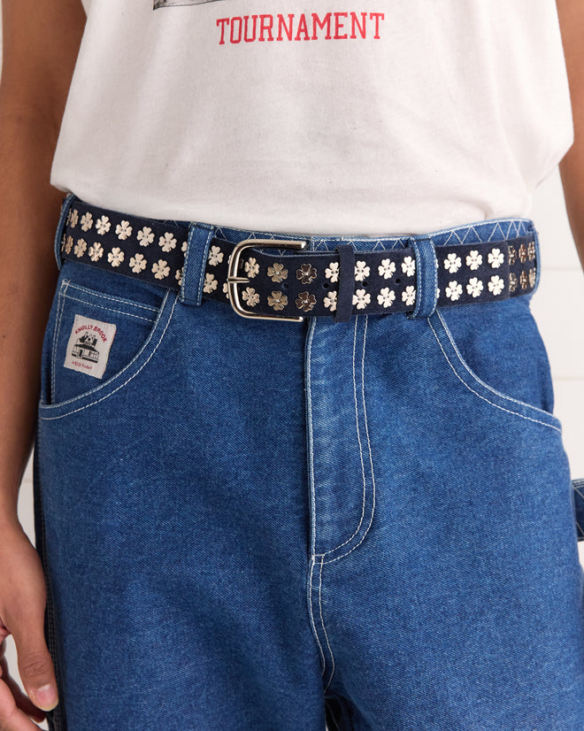 A person in blue jeans and a white shirt completes their look with the Clover Charm Belt - Dark Navy, featuring vintage clover charms and floral designs.