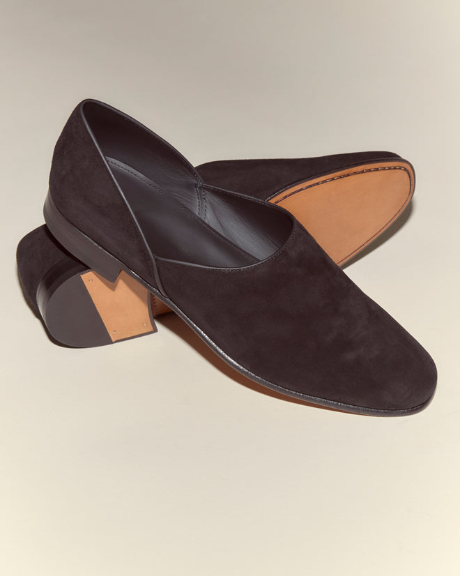 A pair of Suede House Shoes - Black, crafted in Italian suede with tan soles; one shoe is upright while the other rests on its side.