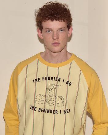 A young man with curly red hair wears the Summertime Stripe Baseball Tee in yellow and cream with the text 