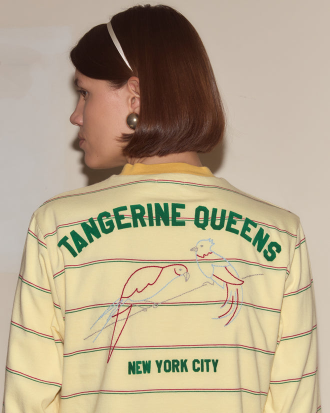Woman with a bob haircut layers the Summertime Stripe Cardigan over a yellow "Tangerine Queens New York City" shirt featuring parrot drawings, creating a playful yet cozy style.