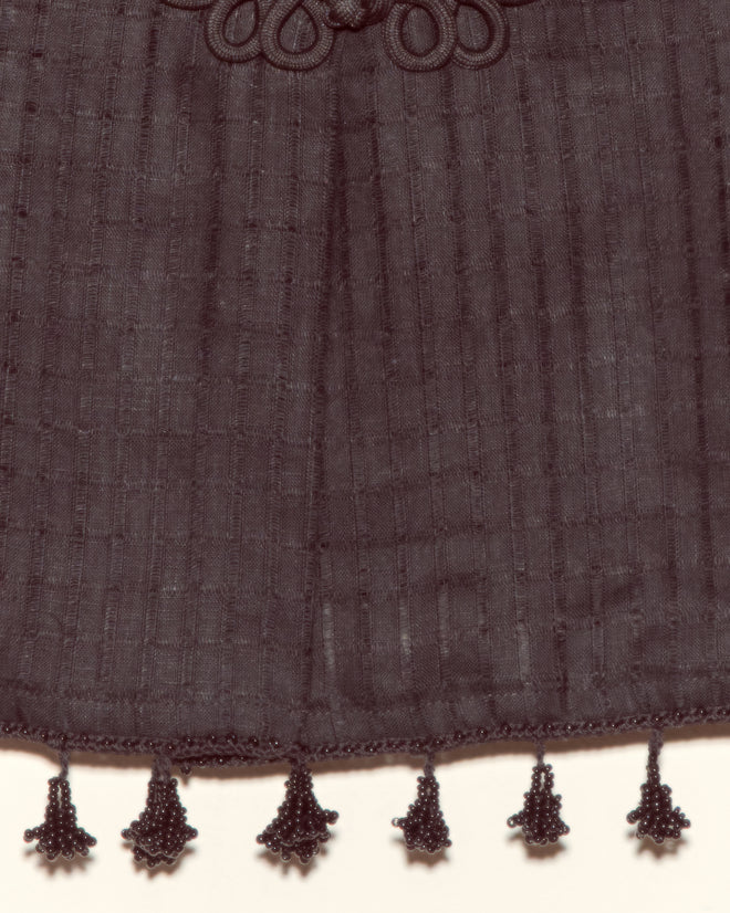 The Surrey Fringe Shirt is a black linen-cotton blouse featuring bead tassels along the edge, shown against a light background.