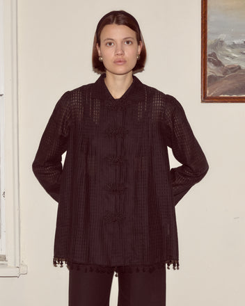 A woman wears the Surrey Fringe Shirt, standing indoors against a beige wall and looking directly at the camera.