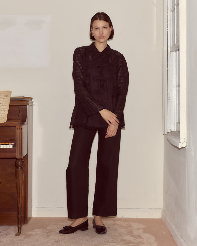 A woman wearing the Surrey Fringe Shirt stands by a piano, looking at the camera in a bright, minimalist room with a window.