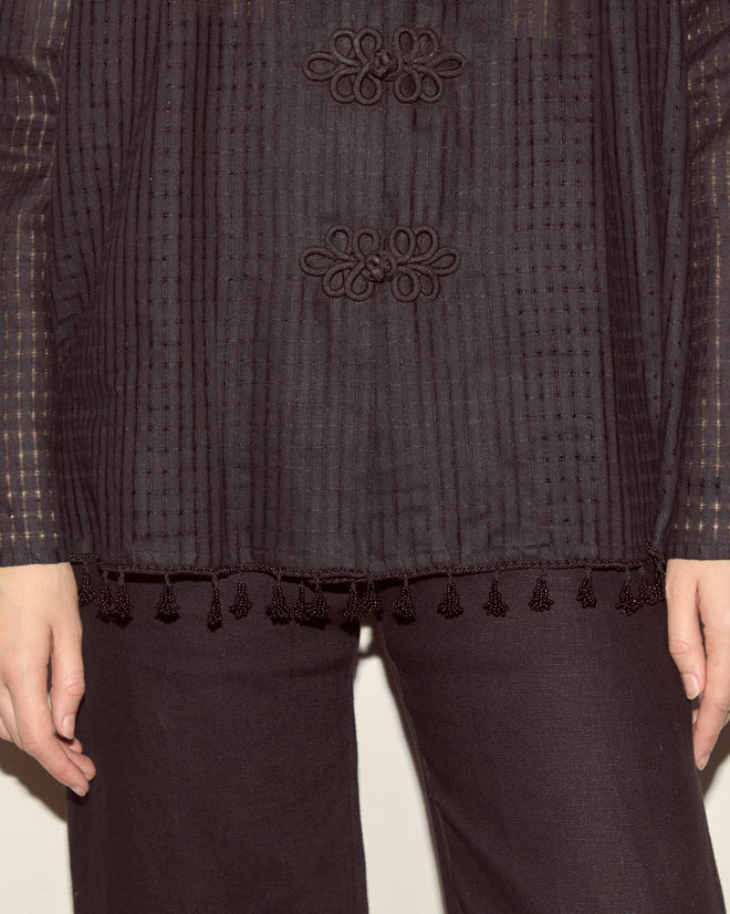 A person wearing the Surrey Fringe Shirt—a black linen cotton top with droplet bead trim at the hem—and black pants, hands at their sides.
