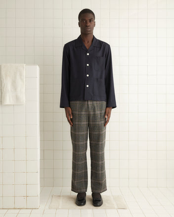 A person in the Swallowtail Overshirt - M and handmade plaid pants stands in a tiled room with a towel hanging nearby.