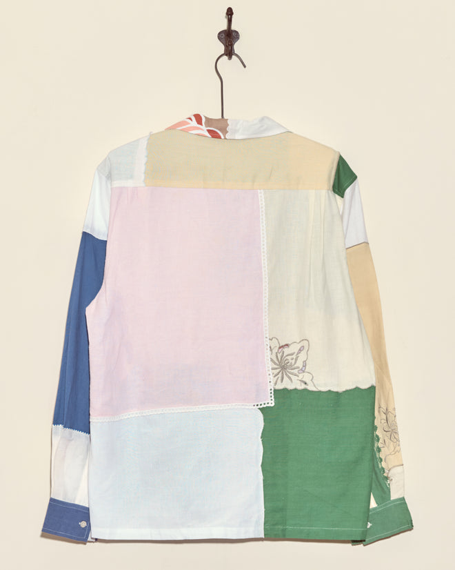 The Sweetpea Napkin Shirt - L/XL, featuring unique pastel patchwork fabric squares, hangs on a wall hook.