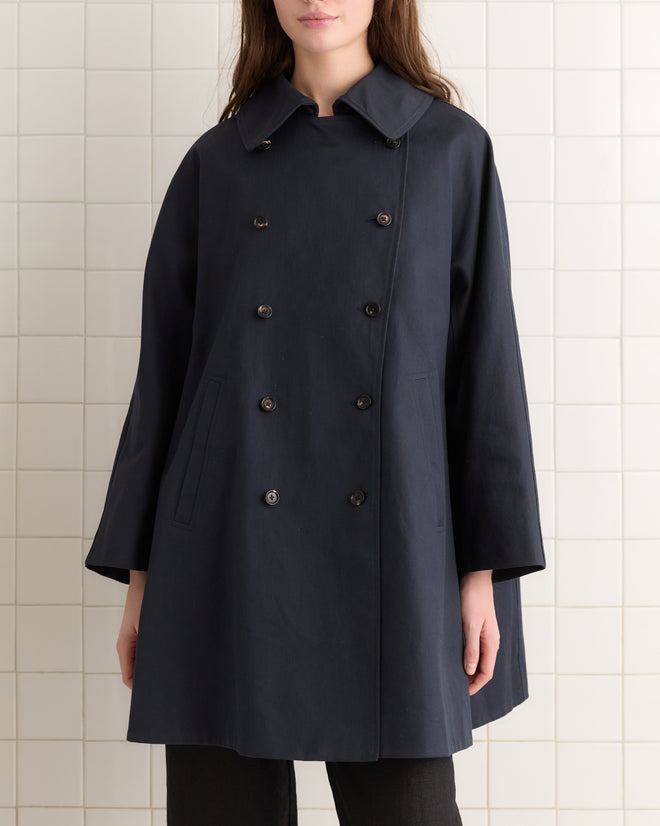 A woman in a chic Waxed Herringbone Peacoat exudes sophistication. The double-breasted coat's stylish design mirrors a classic French peacoat, ideal for those who appreciate timeless elegance.