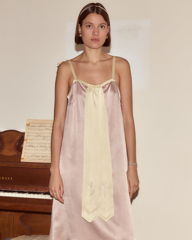A woman in the Sylphid Dress, a lilac pink silk gown, stands before a piano with sheet music on its stand.