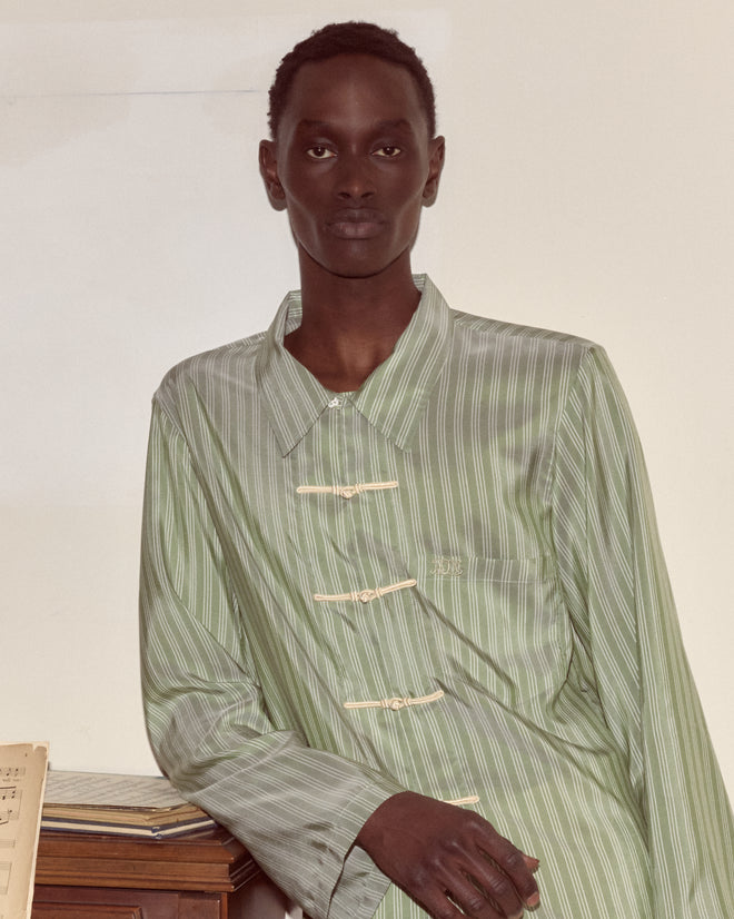 A person wears the Sylvan Stripe Long Sleeve Shirt, leaning on a wooden surface and looking confidently at the camera against a plain background.