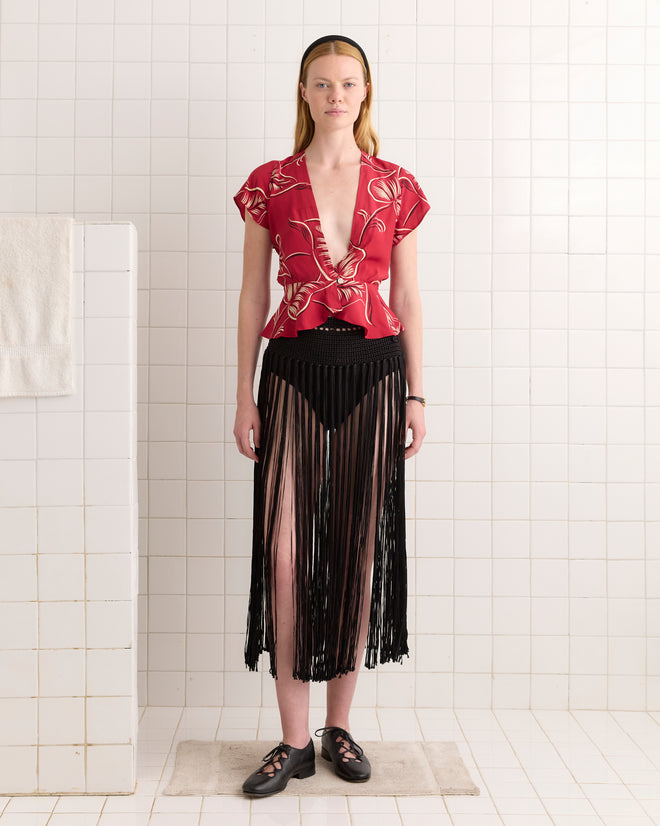 Woman in a red floral top and black Crochet Fringe Skirt stands on a mat in a tiled room with white walls.