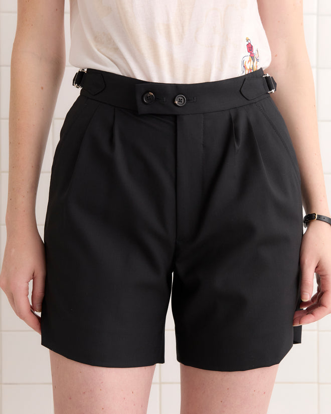Person wearing Tropical Wool Double Button Shorts in black and a white t-shirt, standing against a tiled wall.