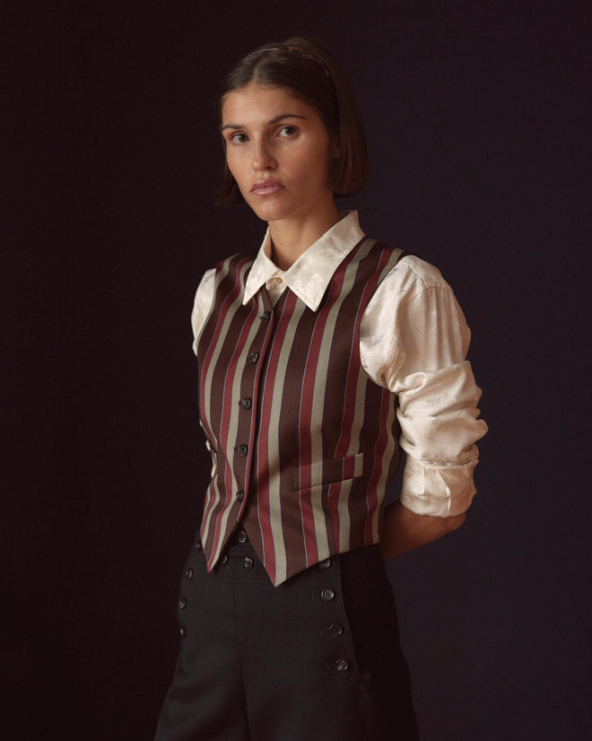 A person in an Arizona Stripe Waistcoat paired with a white shirt stands against a dark background, hands behind their back.