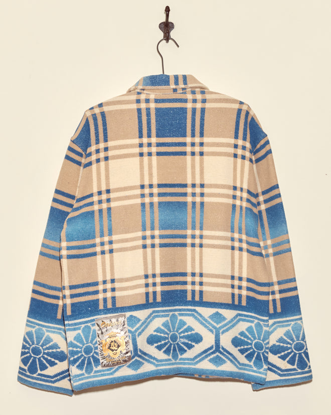 The Tartan Floral Jacket - S/M, a unique brown and blue plaid jacket with a geometric border and patch, crafted from classic midcentury wool, hangs on a wall hook.