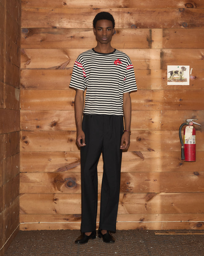 A person wearing the Rib Stripe Training Shirt and black pants stands in a wooden room with a fire extinguisher on the wall.