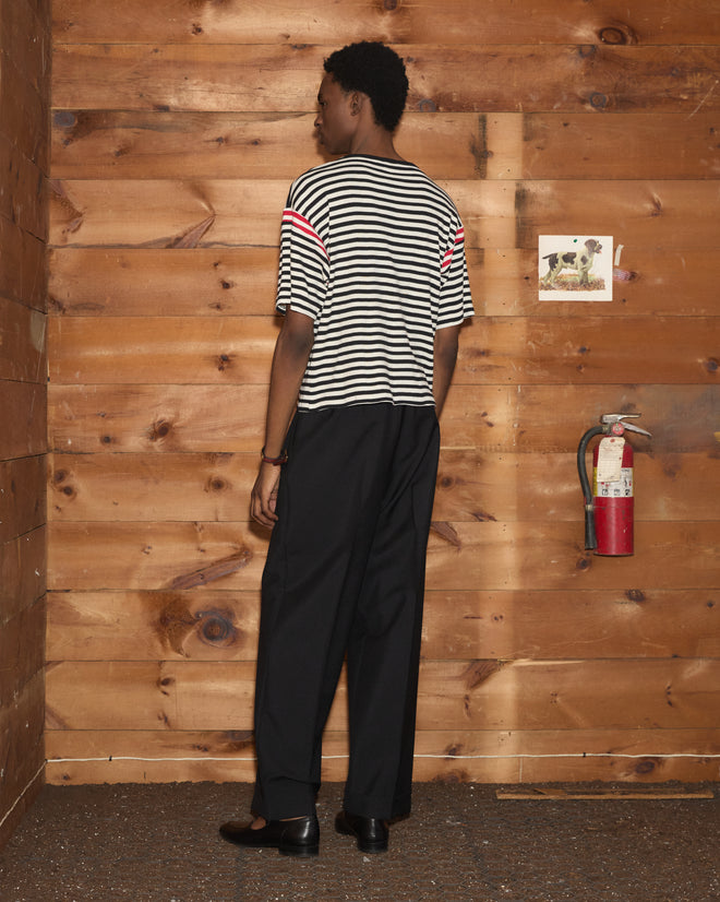 A person wearing the Rib Stripe Training Shirt and black pants stands in a wooden room, facing away from the camera.