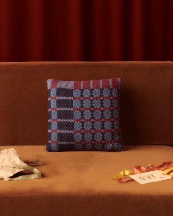 A Berry Bush Pillow on a brown sofa is adorned with colorful ribbons and rests beside an antique coverlet pillow, with a note nearby.