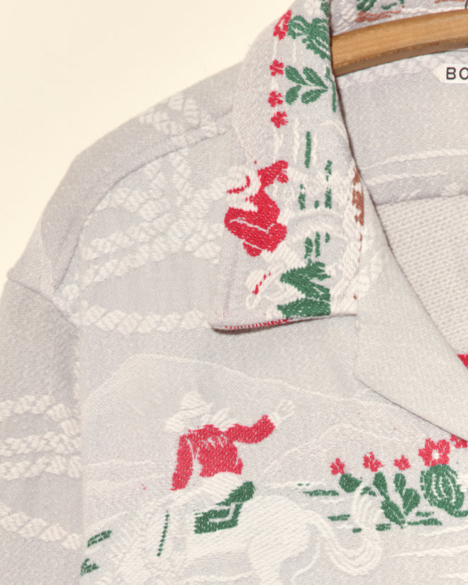 Close-up of the Team Ropers Overshirt - XL, featuring vibrant red and green cowboy and horse patterns on a light background, hanging on a wooden hanger—a unique vintage find.