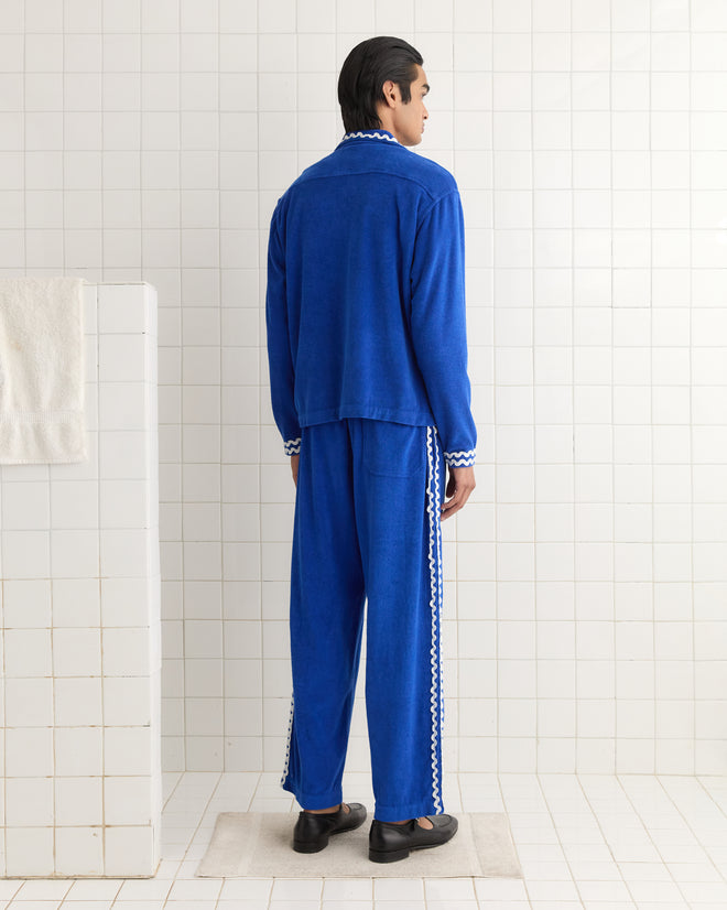 A person in a blue Terry Trim Overshirt stands in a tiled room, back to the camera, with a white towel on a wall rack.