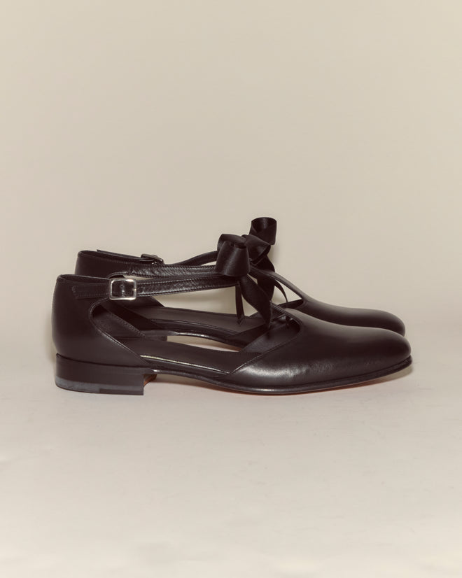 Theater Shoes - Black: Black leather ballet flats featuring ribbon and buckle details, inspired by midcentury dancing shoes, displayed against a plain background.