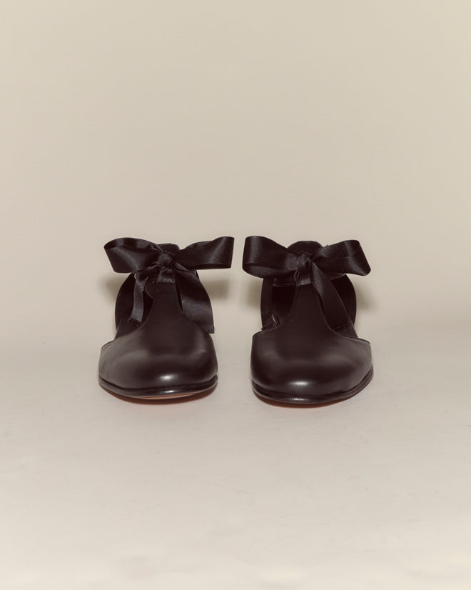 Theater Shoes - Black: Black leather T-strap shoes with large black ribbon bows, inspired by midcentury dancing shoes, displayed on a plain light background.