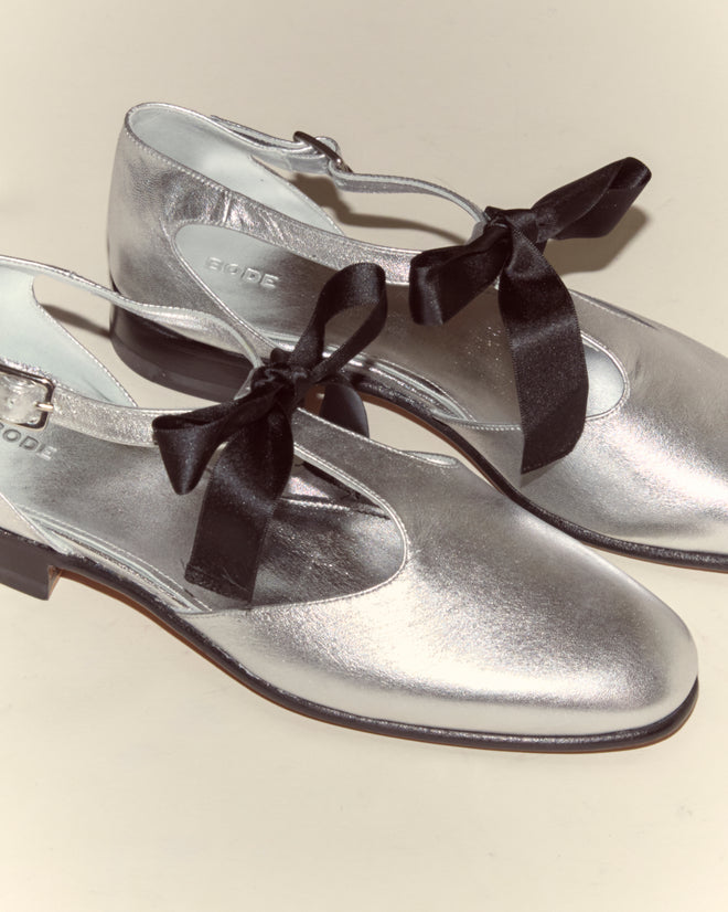 Theater Shoes - Silver: Metallic leather Mary Jane shoes with black ribbon bows, inspired by classic midcentury dancing styles, shown on a light background.