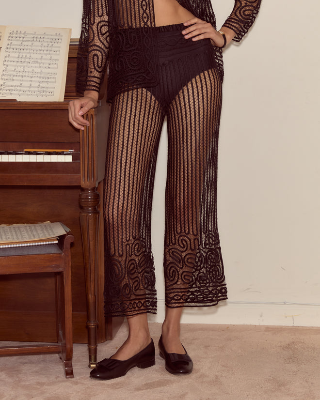 Wearing Threadwork Pants, a person in a sheer black outfit stands by a piano with sheet music, visible from the shoulders down.