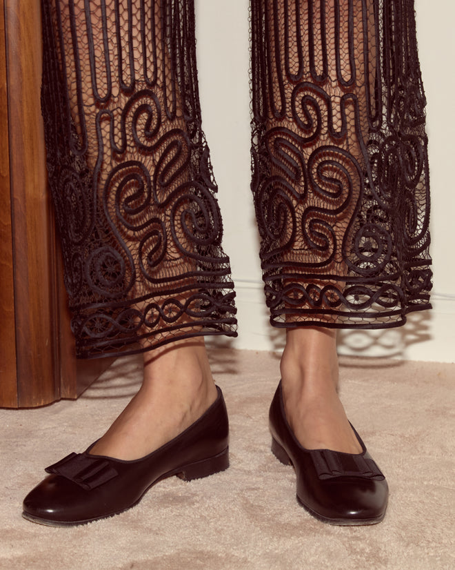 A woman stands on a beige carpet wearing black loafers and elegant black Threadwork Pants.