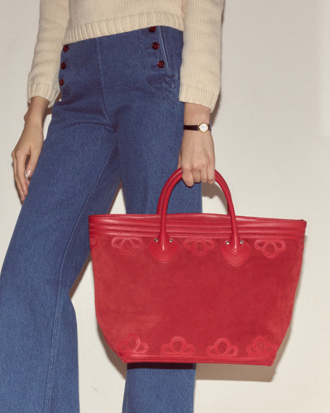Woman in blue wide-leg jeans carries the Trefoil Tote - Red, paired with a cream sweater and watch, creating a chic look with a boxy silhouette.