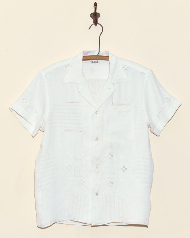 The Trellis Block Short Sleeve Shirt in XS, featuring subtle cutwork embroidery, hangs on a wooden hanger against a beige wall.