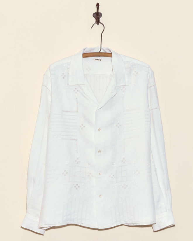 The Trellis Block Long Sleeve Shirt (L) features delicate cutwork patterns and button-up design, displayed on a hanger against a cream wall—an elegant, unique wardrobe piece.