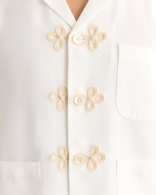 The Trillium Long Sleeve Shirt in cream is a 1940s-inspired silk crepe top featuring decorative knot buttons, trompe l'oeil frog closures, and two front pockets.