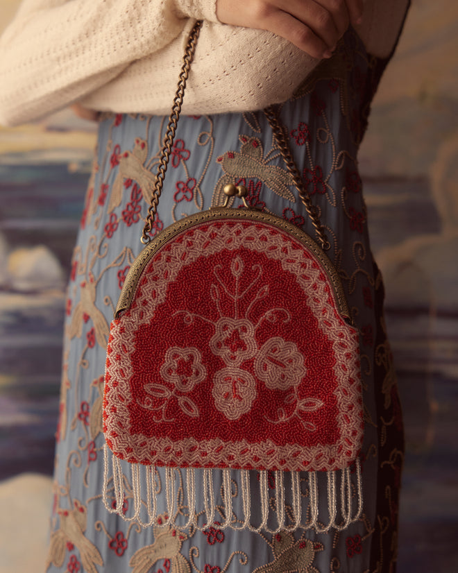 Amrita Beaded Bag, showcasing a vintage red and white floral pattern, elegantly displayed on a snowy surface with a decorative background.