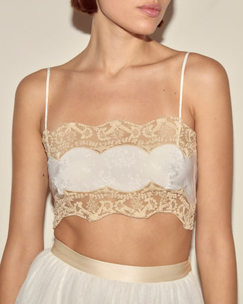 Woman wearing the Trousseau Lace Bra, a cream lace bralette crop top with thin straps, paired with a white skirt; shown from the shoulders down.