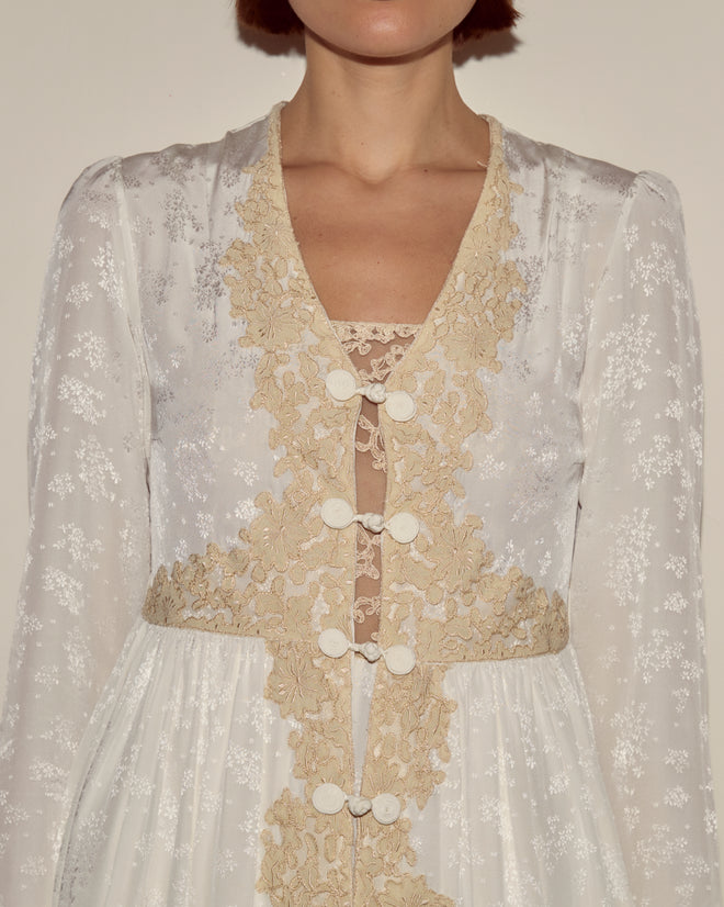 A woman wearing the Trousseau Lace Dress in cream, featuring vintage-inspired jacquard silk, beige lace trim, and white button details.