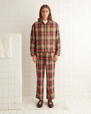 A person with long hair stands in a white-tiled room, donned in the Truro Plaid Jacket and matching pants made from virgin wool, along with black shoes.