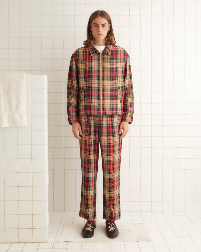 A person with long hair stands in a white-tiled room, donned in the Truro Plaid Jacket and matching pants made from virgin wool, along with black shoes.