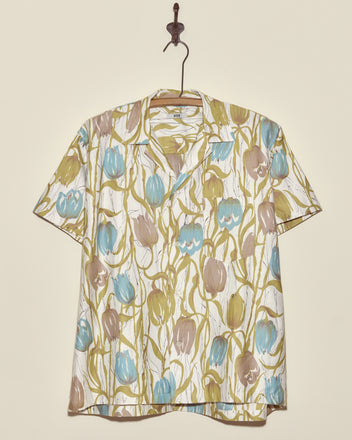 The Tulip Watercolor Shirt - M/L is a unique short-sleeved shirt featuring blue, brown, and green tulip patterns, crafted in New York and displayed on a metal hook.