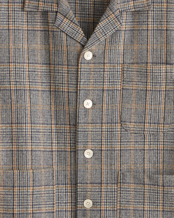 The Tumbleweed Plaid Overshirt - M, with its gray plaid pattern that echoes 1960s suiting fabric and is made from 100% wool, hangs on a hanger against a white tiled wall.