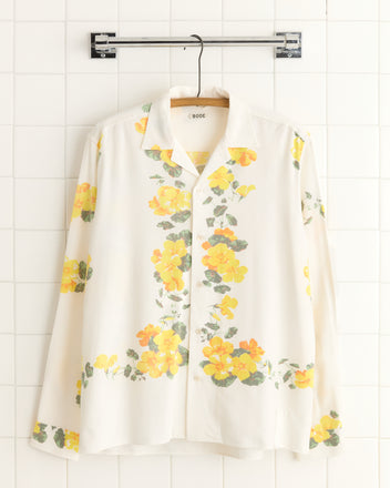 Tuscan Gold Flower Shirt (S/M) featuring a golden floral pattern on white, hangs on a wooden hanger against a tiled wall.