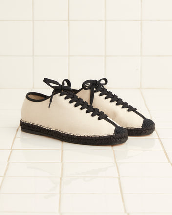 A pair of Tennis Espadrilles - Natural with black laces and soles, set on a tiled floor.