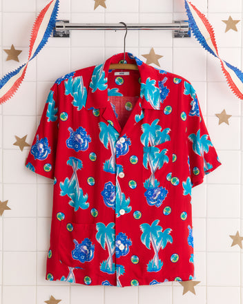 The Ukulele Tune Shirt features blue tropical designs on red fabric made from rare deadstock yardage, displayed against a white tiled wall with star decorations.