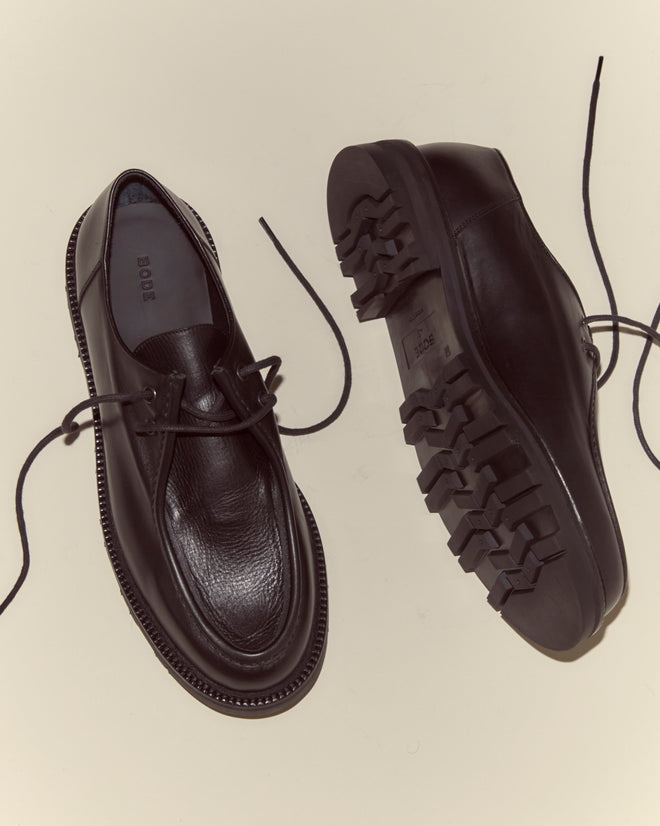 A pair of University Shoes - Black, made from black Napa leather with thick rugged soles and untied laces in classic Italian style, rests on a light background.