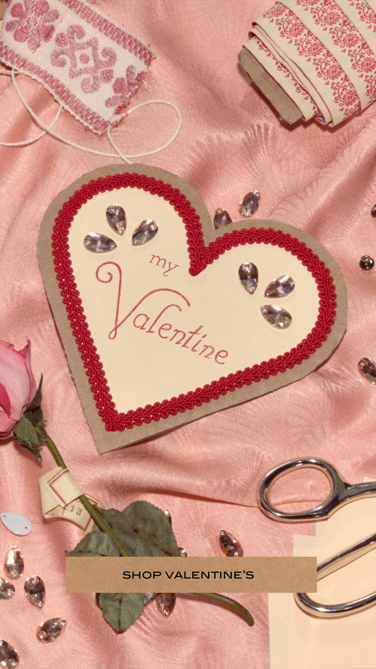 An assortment of pink and red fabrics and ribbons scattered about for a Valentine's Day themed image. In the center is a heart shaped card that sys, 