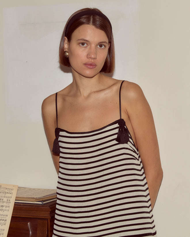 Woman wearing the Velvet Bannister Dress with pearl earrings and a headband, standing indoors beside sheet music.