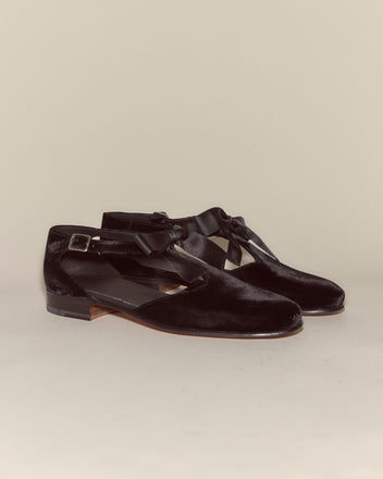 Velvet Theater Shoes - Black feature black velvet, ankle straps, ribbon bows, and low heels, bringing classic midcentury ballet style to modern footwear on a neutral background.