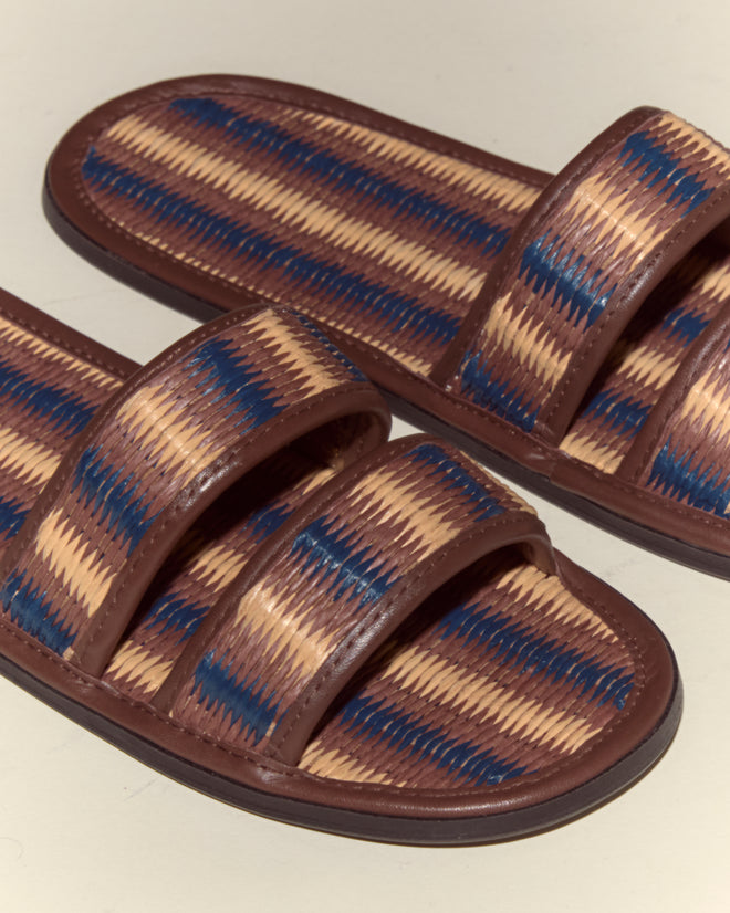 The Duotone Summer Slides - Brown/Blue feature brown, beige, and blue striped woven patterns with two straps each—ideal chic raffia leather slides for stylish warm-weather looks.