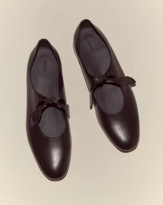 The Verbena Shoes - Black are classic Mary Jane-style ballet flats in black leather, featuring bow accents on top and displayed on a neutral background.