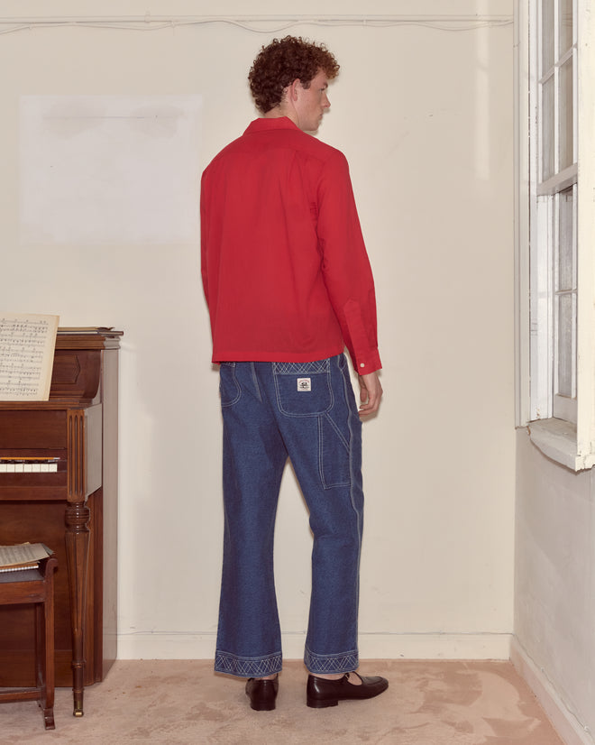 A person wearing the Voile Long Sleeve Shirt - Red and blue jeans stands indoors near a piano, facing away from the camera.