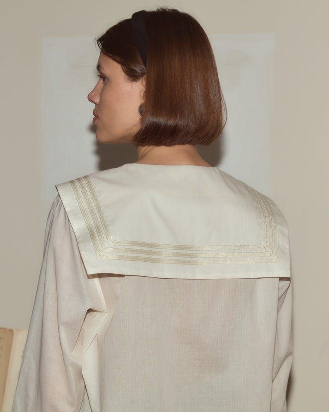 Woman with short brown hair wearing the Voile Marina Shirt with a sailor collar, facing away from the camera against a pale wall.