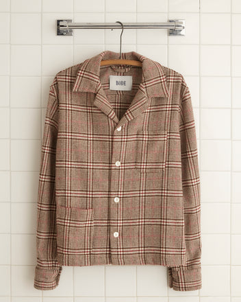 A unique Warm Glen Overshirt in size L/XL, made from 1960s suiting fabric with a collar and buttons, hangs gracefully on a hanger against a tiled wall.